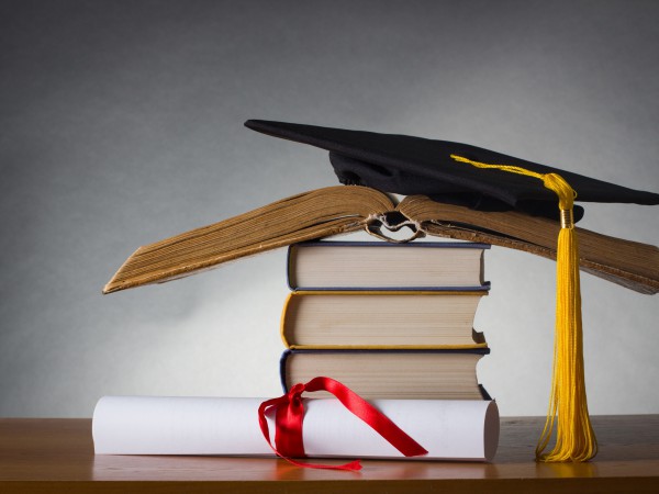 mortarboard and graduation scroll on a stack of battered book