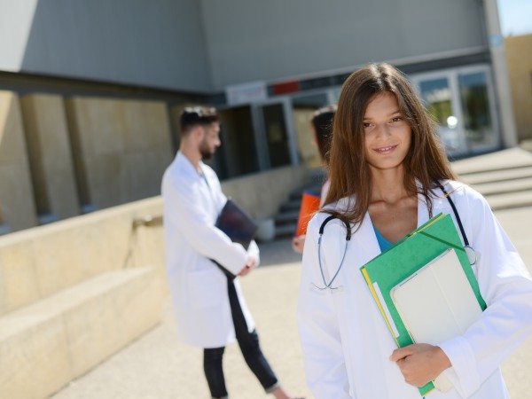 portrait of attractive cheerful young medical student woman outdoor in front of hospital university campus